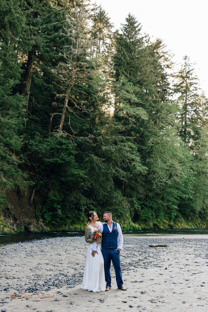 elopement couple standing on a rocky shore with lush forest in the backdrop