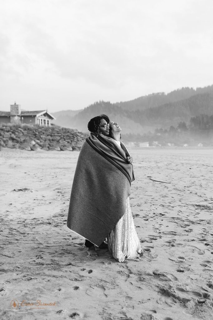 romantic elopement couple cozying under a blanket at the beach shore in Oregon