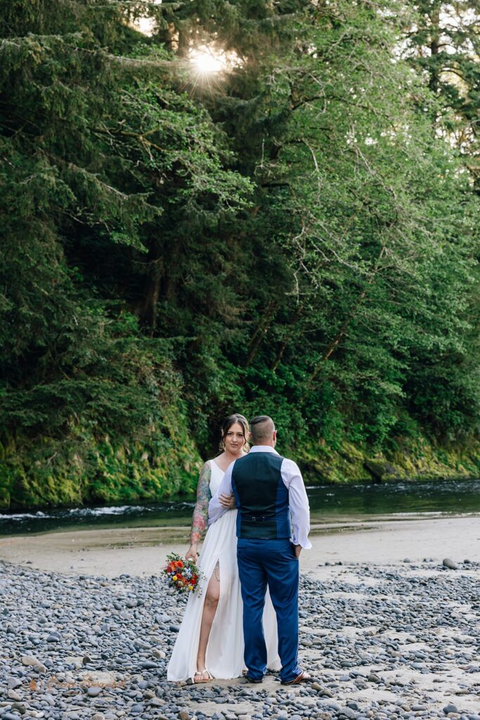 elopement couple standing on a rocky shore with lush forest in the backdrop