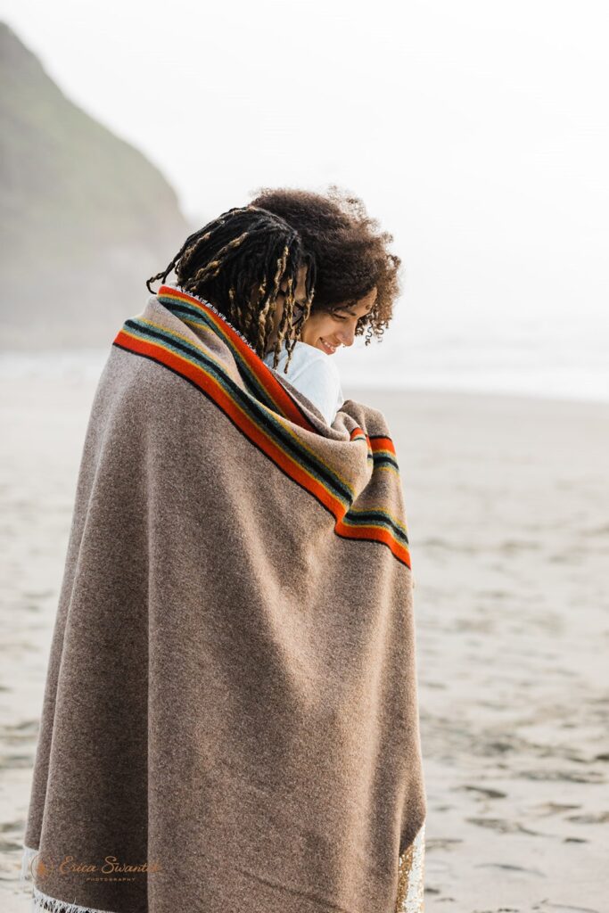 romantic elopement couple cozying under a blanket at the beach shore in Oregon