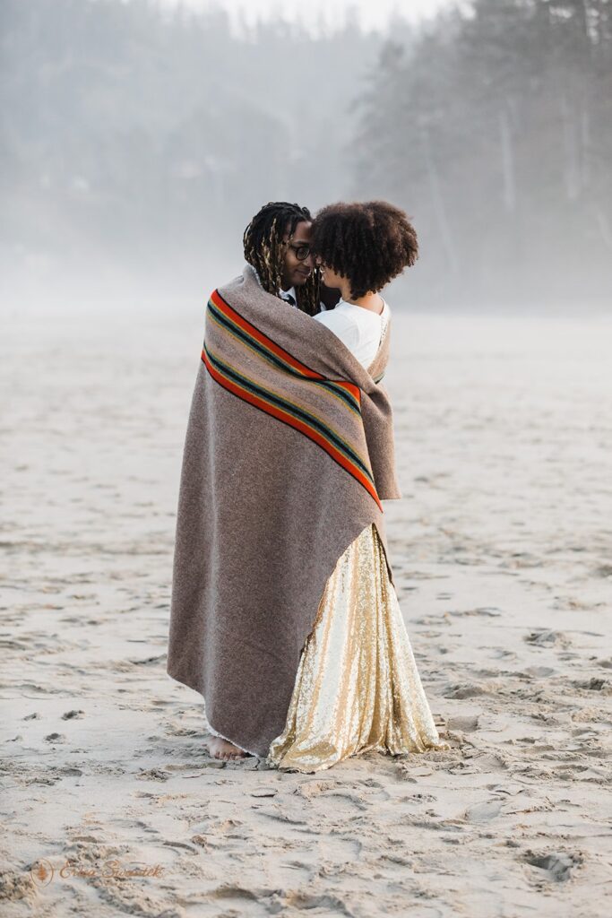 romantic elopement couple cozying under a blanket at the beach shore in Oregon