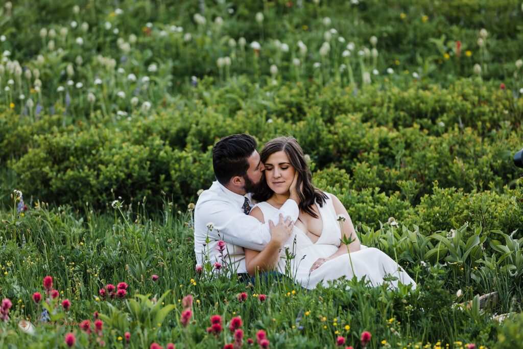 romantic bride and groom sitting in a lush green meadow surrounded by wildflowers