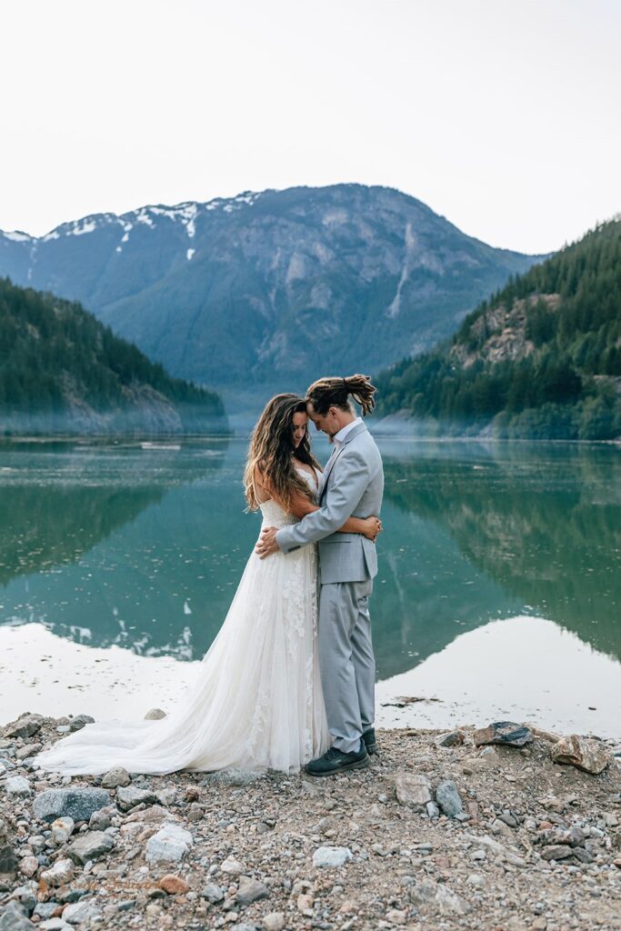 bride and groom standing at a crystal clear lake shore with mountains in the backdrop