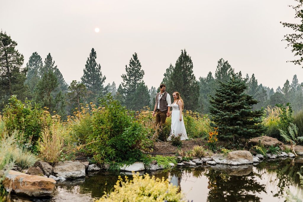 bride and groom walking in wildflowers with an eerie sunset from a forest fire during their PNW elopement