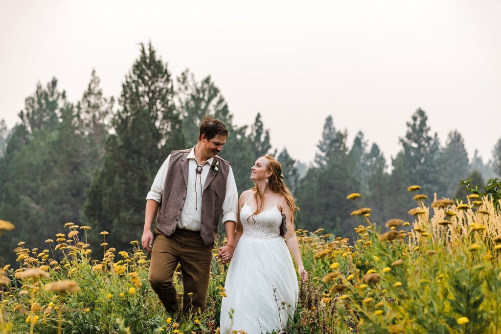 bride and groom walking in wildflowers with an eerie sunset from a forest fire during their PNW elopement