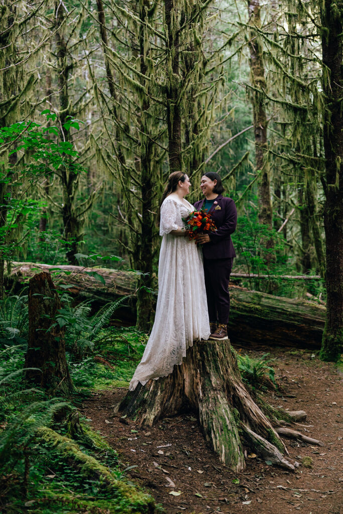 two brides stand on a stump in the forest in oregon.
