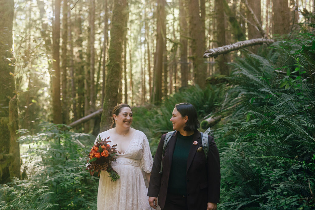 A couple hikes through the forest in their wedding clothes.
