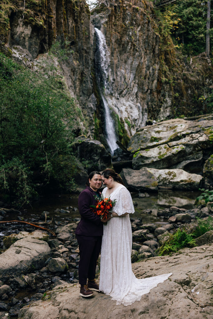 two brides pose in front of an Oregon waterfall.