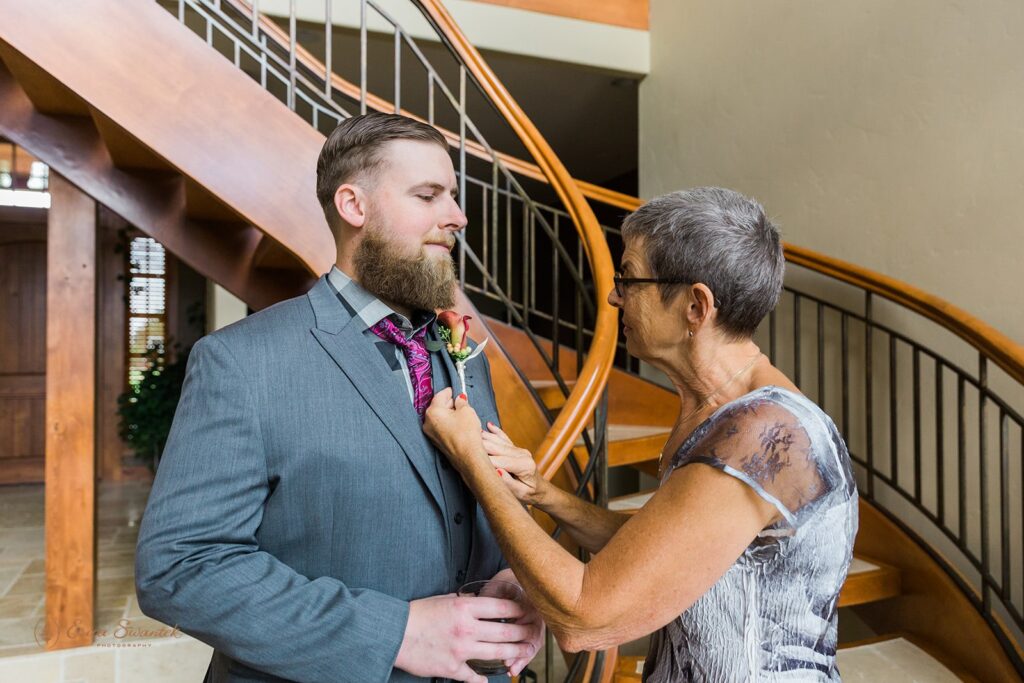 A groom's mom pins his boutonniere on his suit jacket. 