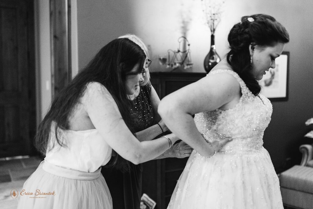 A bride's sister and mother help her into her wedding dress. 