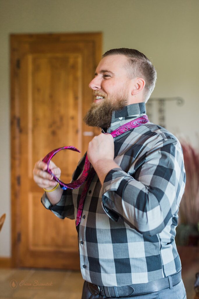 groom ties his tie while smiling