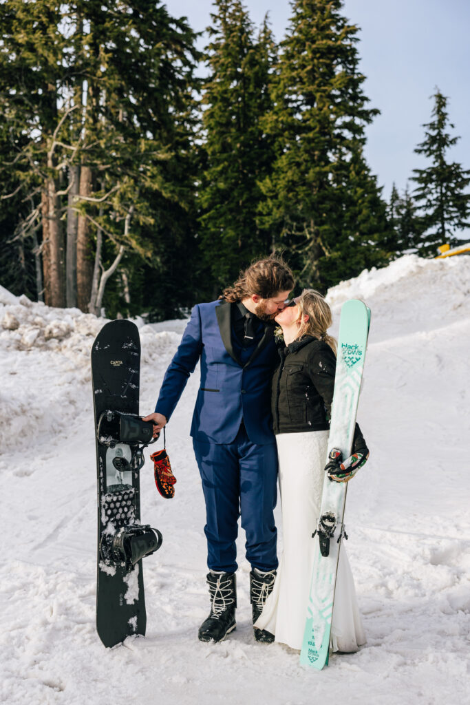 A couple kisses holding their snowboard and skis at the Mt. Hood Meadows ski resort elopement in Oregon. 