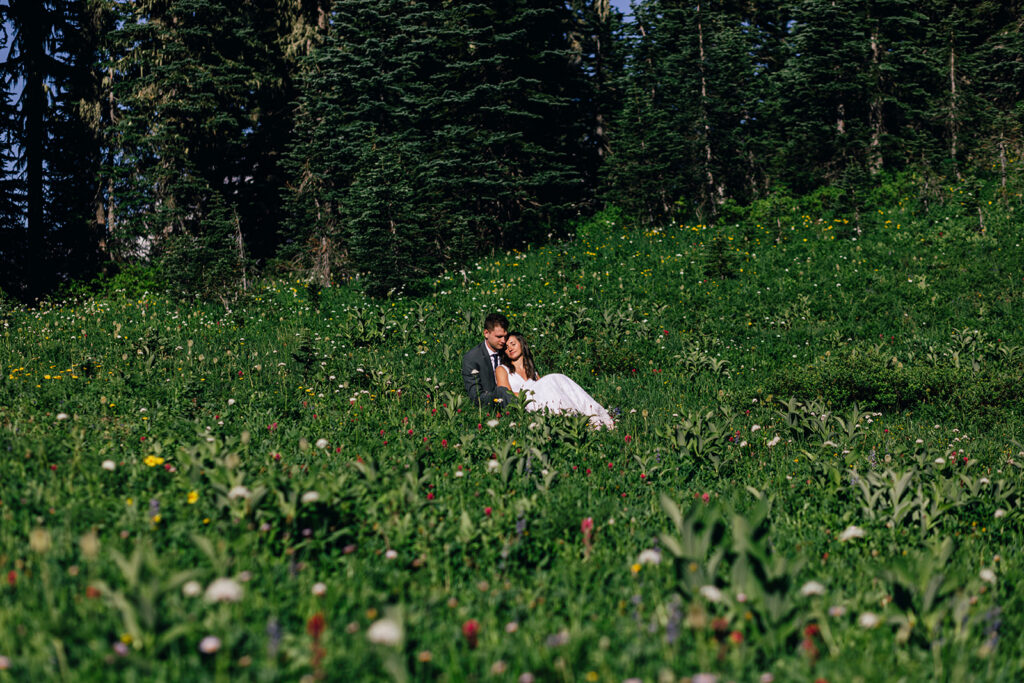 A couple sits among the wildflowers at their Mt. Rainier elopement.