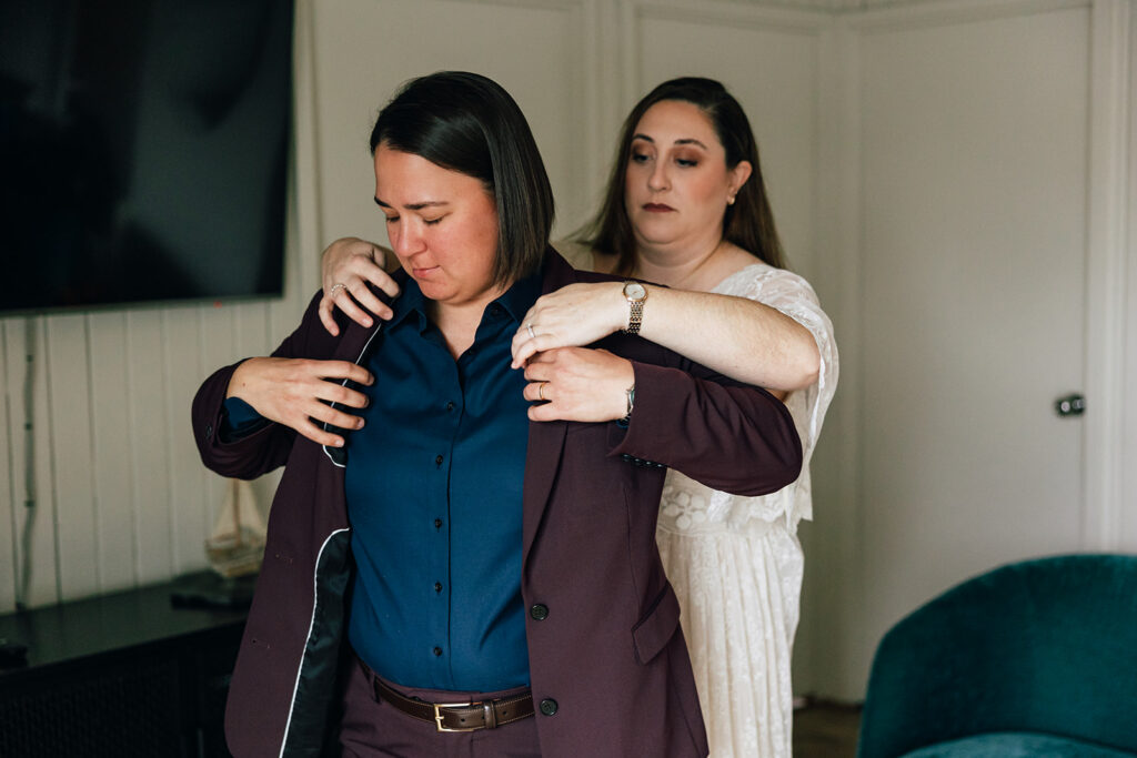 A couple helps each other get dressed on their elopement day on the Oregon Coast.