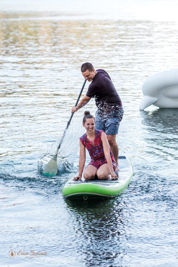 fun couple paddleboarding on a lake for their engagement session