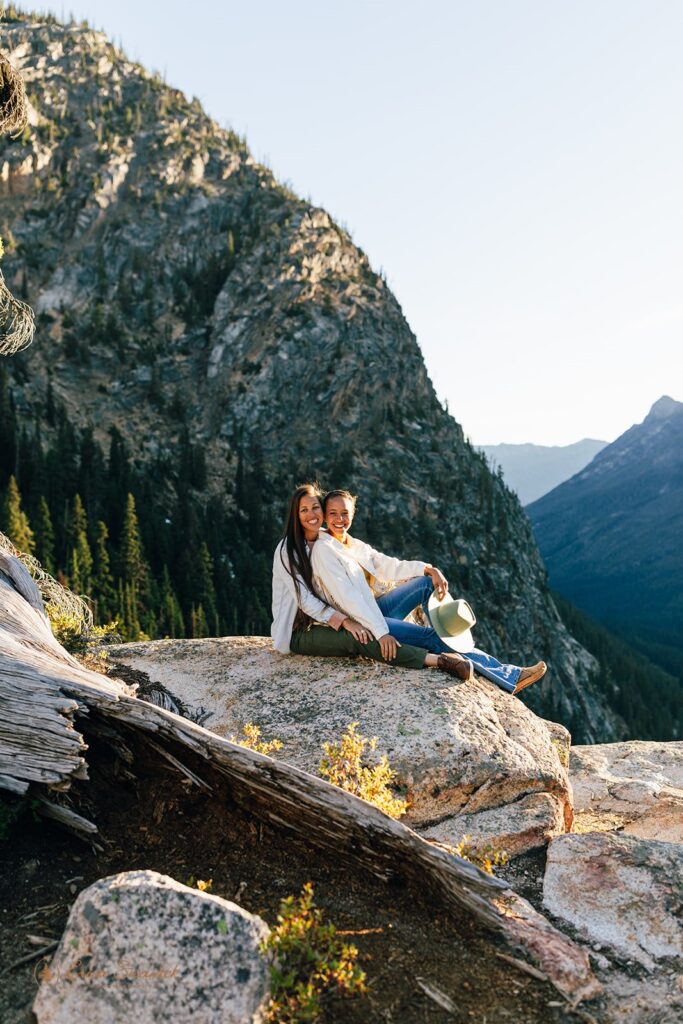 candid engaged couple sitting on a rock with stunning mountain views in the backdrop