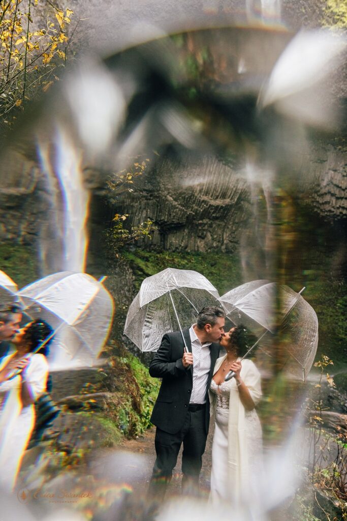 bride and groom under clear umbrellas during their rainy PNW elopement with waterfall backdrop