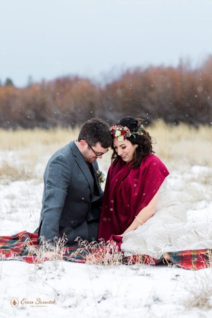 newly weds sitting on a picnic blanket surrounded by snow