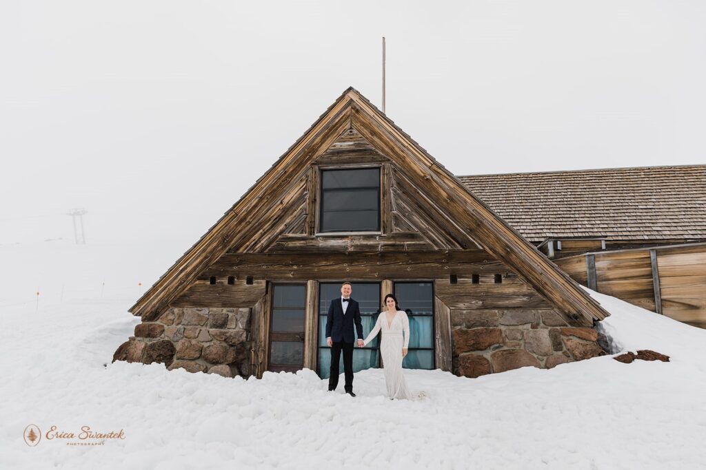 bride and groom posing in the snow with a rustic lodge in the backdrop