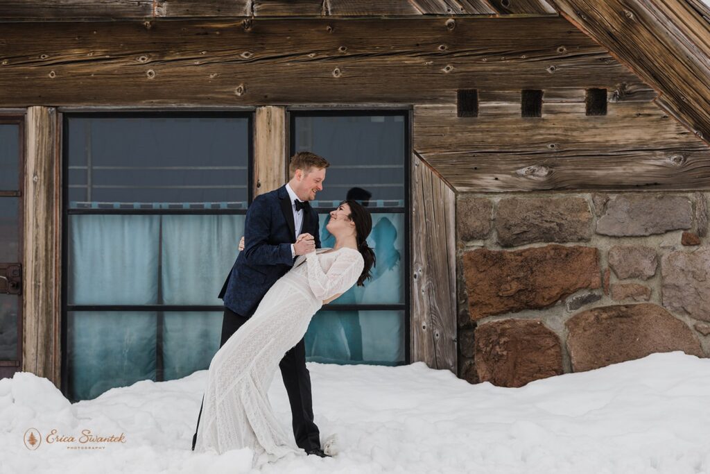 bride and groom dip kiss by a rustic lodge in PNW