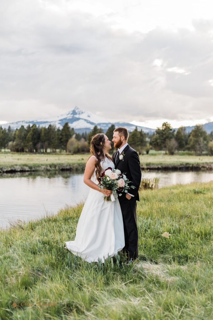 beautiful elopement couple posing in a lush grassy field with mountain backdrops in the PNW