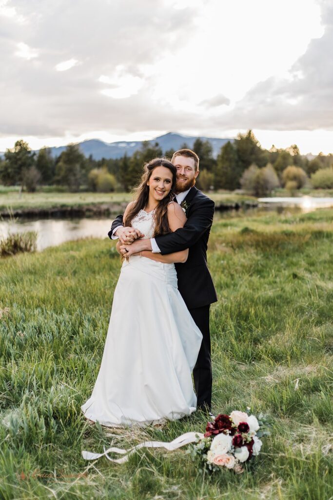 beautiful elopement couple posing in a lush grassy field with mountain backdrops in the PNW