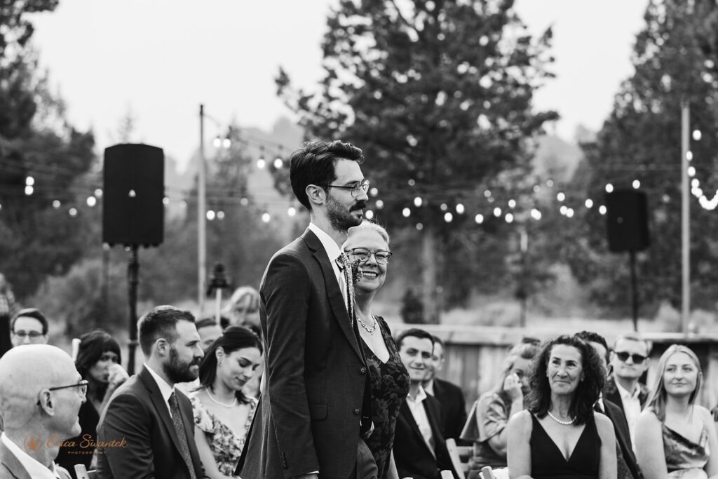 The groom walks arm-in-arm with his mother while smiling at guests during the wedding ceremony