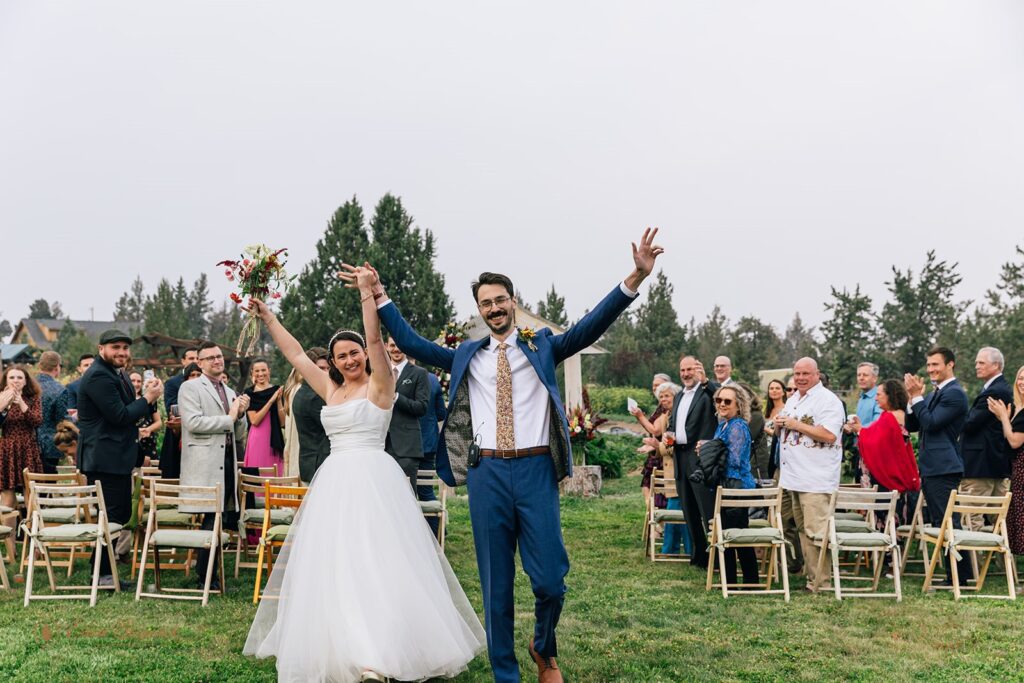 fun and cheerful wedding couple exiting their ceremony as guests cheer on in the backdrop