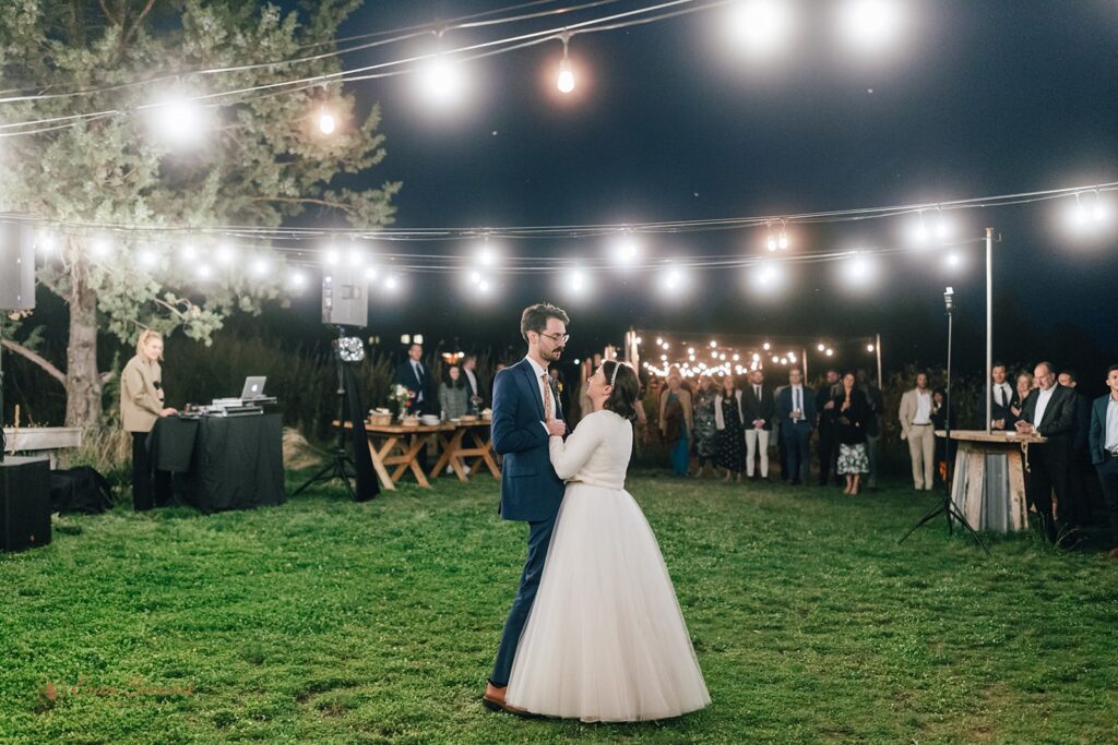 The bride and groom share their first dance under string lights at their outdoor wedding reception