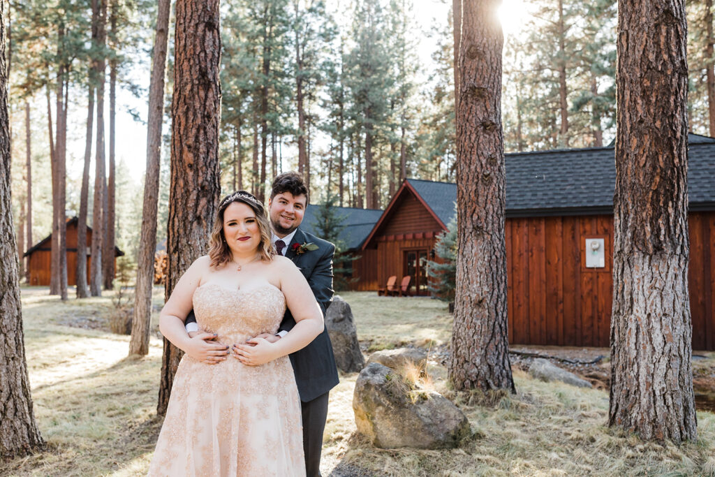 wedding couple posing surrounded by tall trees with rustic lodges in the backdrop