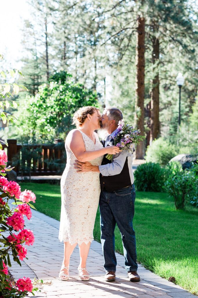 bride and groom kissing on a paved trail surrounded by lush greenery