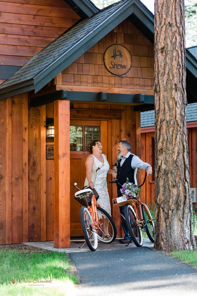 elopement couple with bikes standing against the rustic fivepine lodge wedding venue