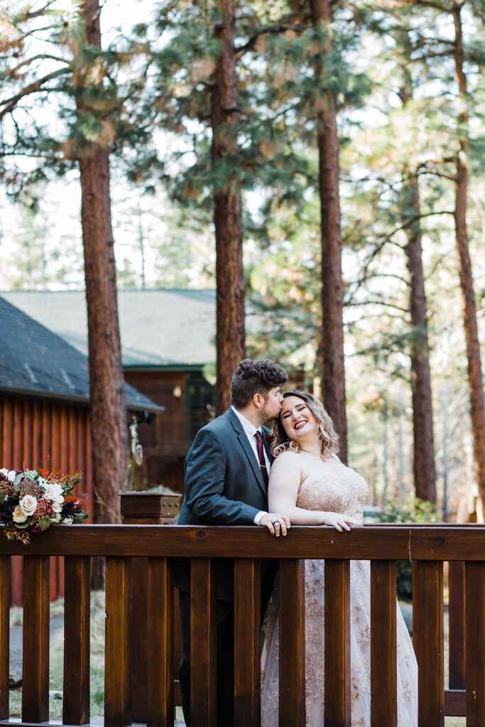 groom kissing bride's forehead with the FivePine Lodge wedding venue peeking in the backdrop