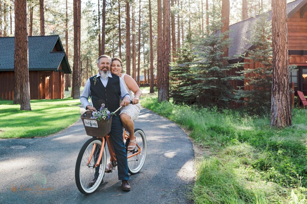 bride and groom riding bikes alongside the cozy cabins of fivepine lodge wedding venue