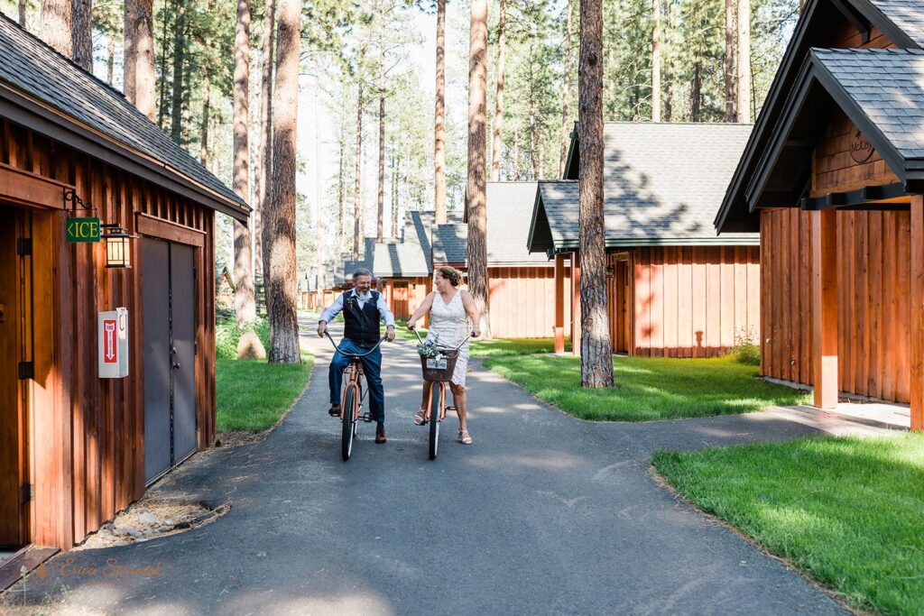 bride and groom riding bikes alongside the cozy cabins of fivepine lodge wedding venue