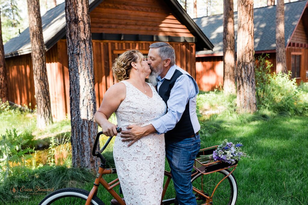 bride and groom riding bikes alongside the cozy cabins of fivepine lodge wedding venue