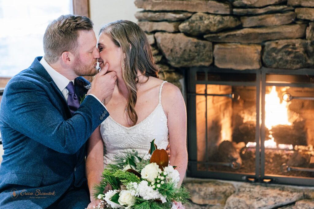 bride and groom kissing by a cozy fireplace