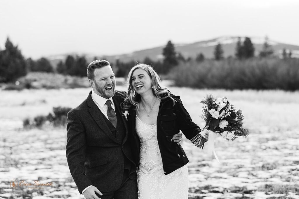 bride and groom walking through a snowy field with mountains in the backdrop