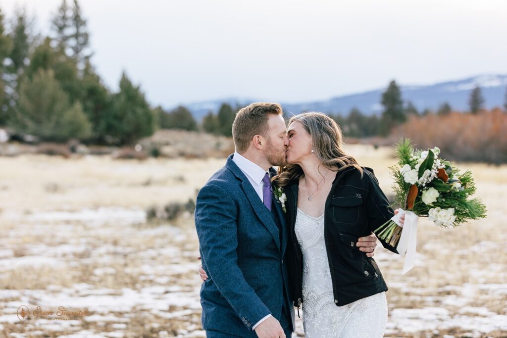 bride and groom walking through a snowy field with mountains in the backdrop