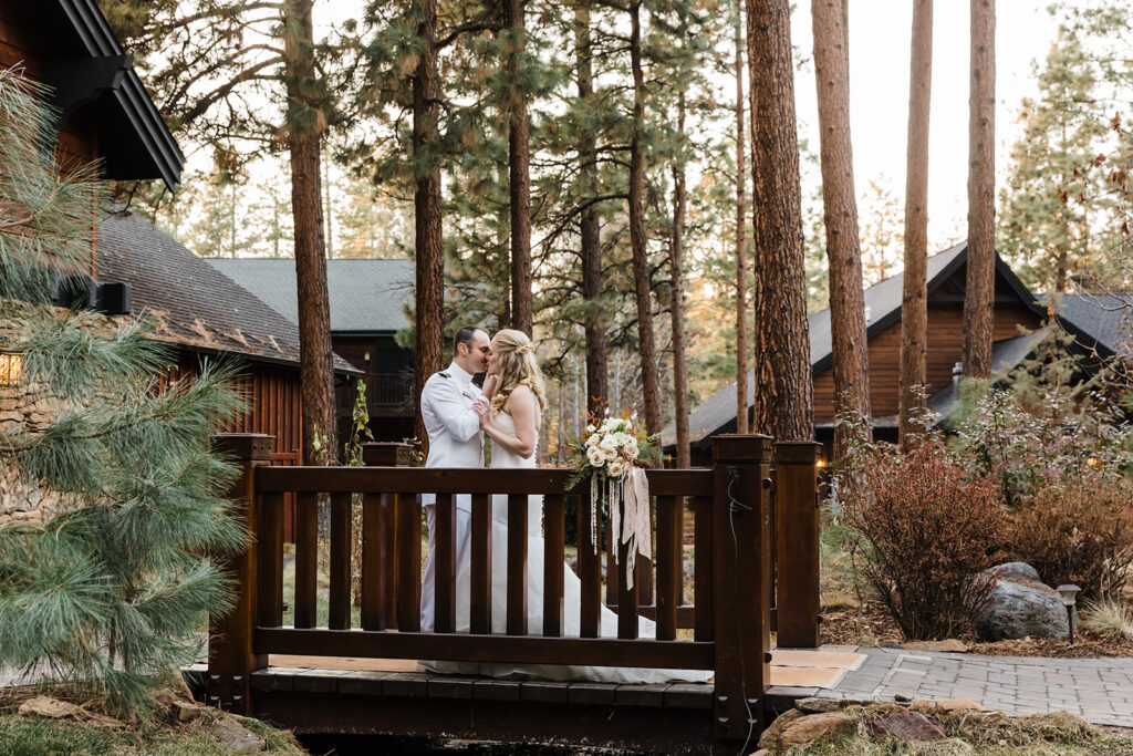 wedding couple kissing on a cute small wooden bridge with rustic lodges in the backdrop