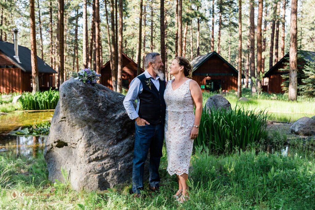 wedding couple posing surrounded by tall trees with rustic lodges in the backdrop