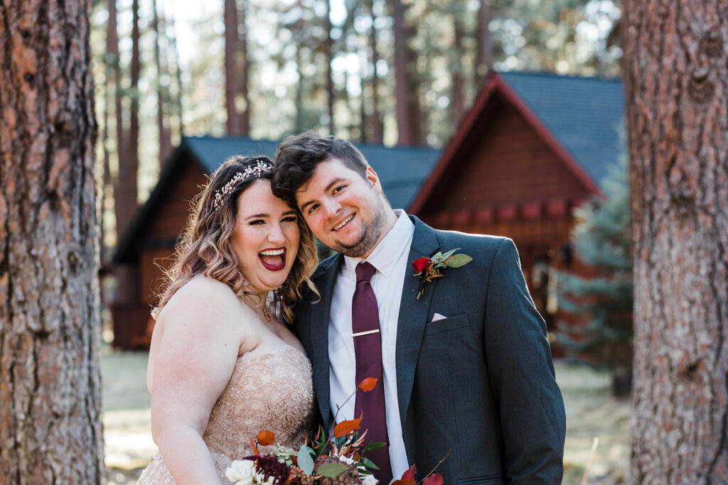 bride and groom with a forest and cozy cabins in the backdrop