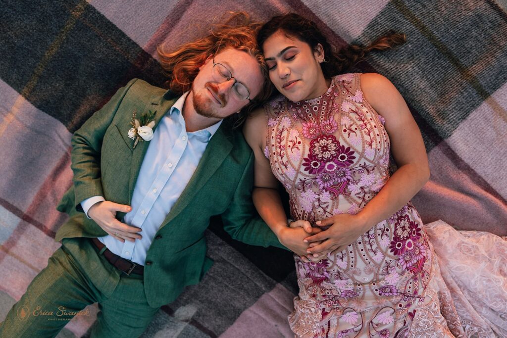 bride and groom laying on their picnic blanket holding hands