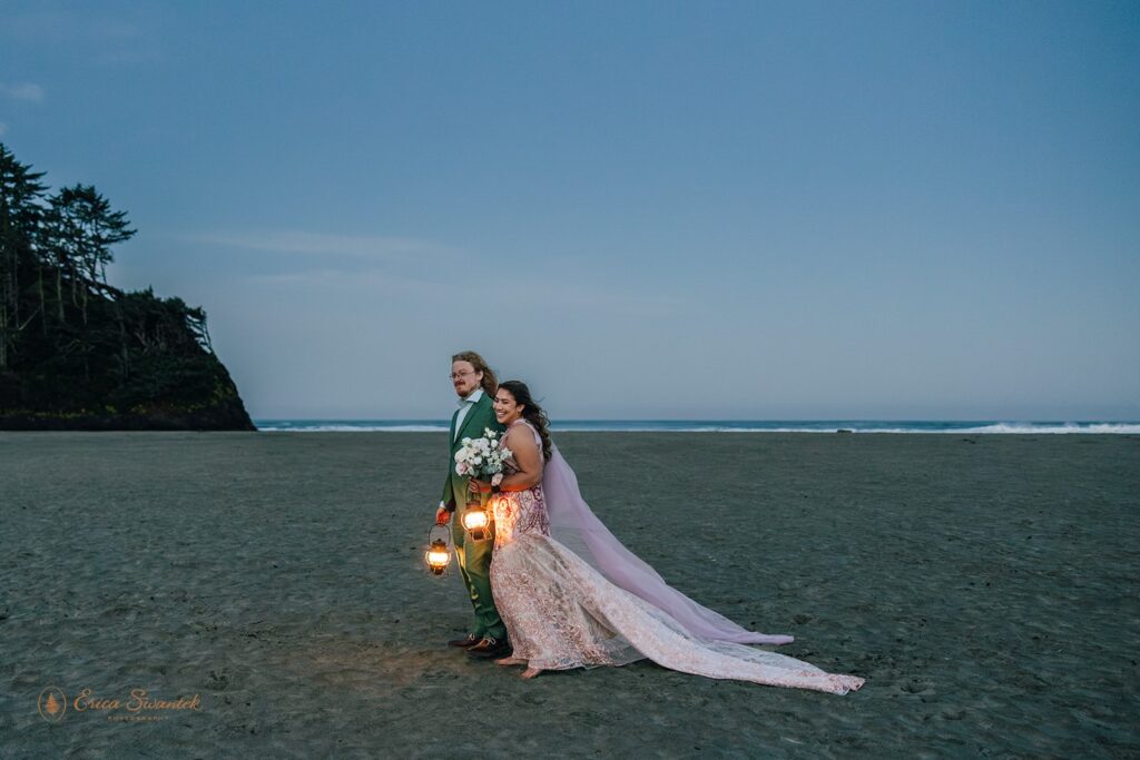 bride and groom carrying lanterns at the beach during sunrise