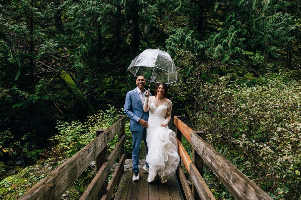 rainy waterfall elopement day in oregon, couple walking under a clear umbrella