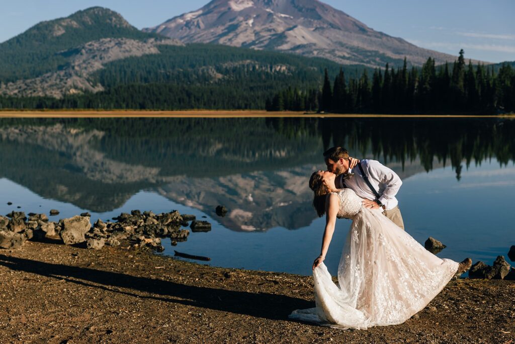 bride and groom kiss by a clear lake with mountain backdrops during their sparks lake elopement day