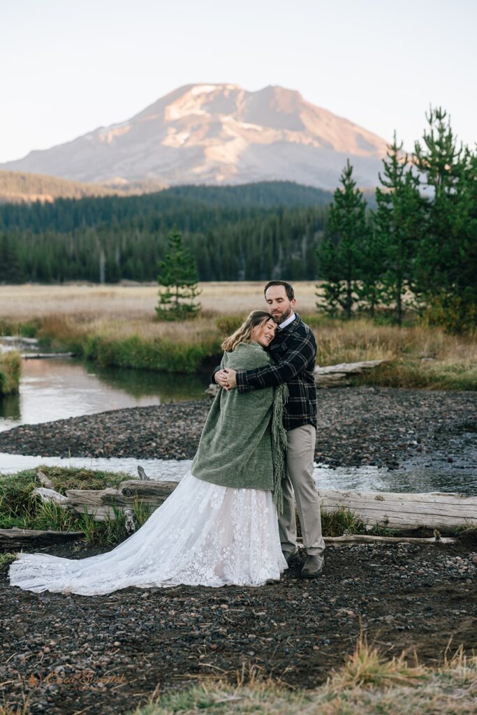 bride and groom walking along the shore of Sparks Lake with mountain views in Oregon