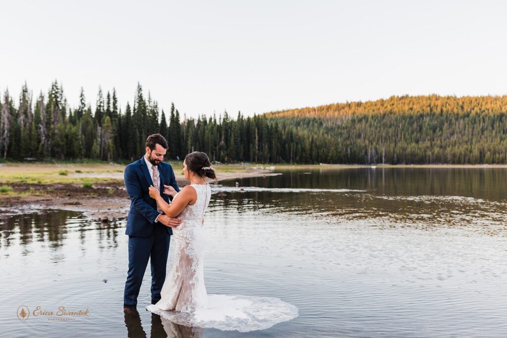 bride and groom standing in the water with mountain and forest views in the backdrop