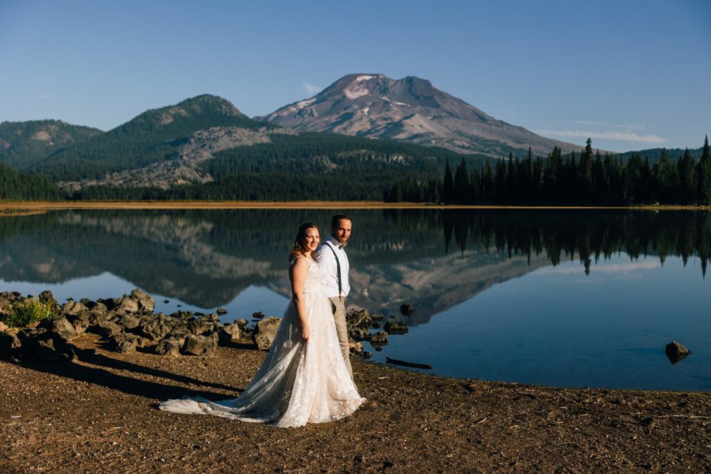 bride and groom walking along the shore of Sparks Lake with mountain views in Oregon