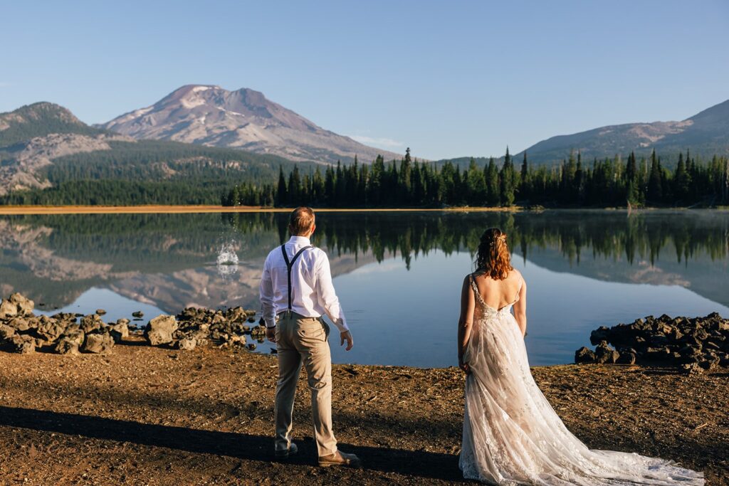 bride and groom walking along the shore of Sparks Lake with mountain views in Oregon